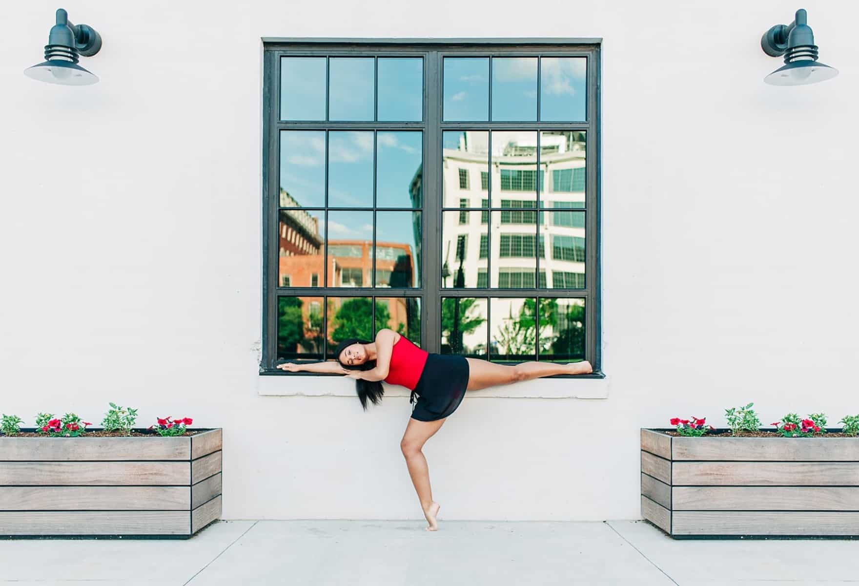 Ballet dancer in a red shirt performing in front of a window, with flowers on each side