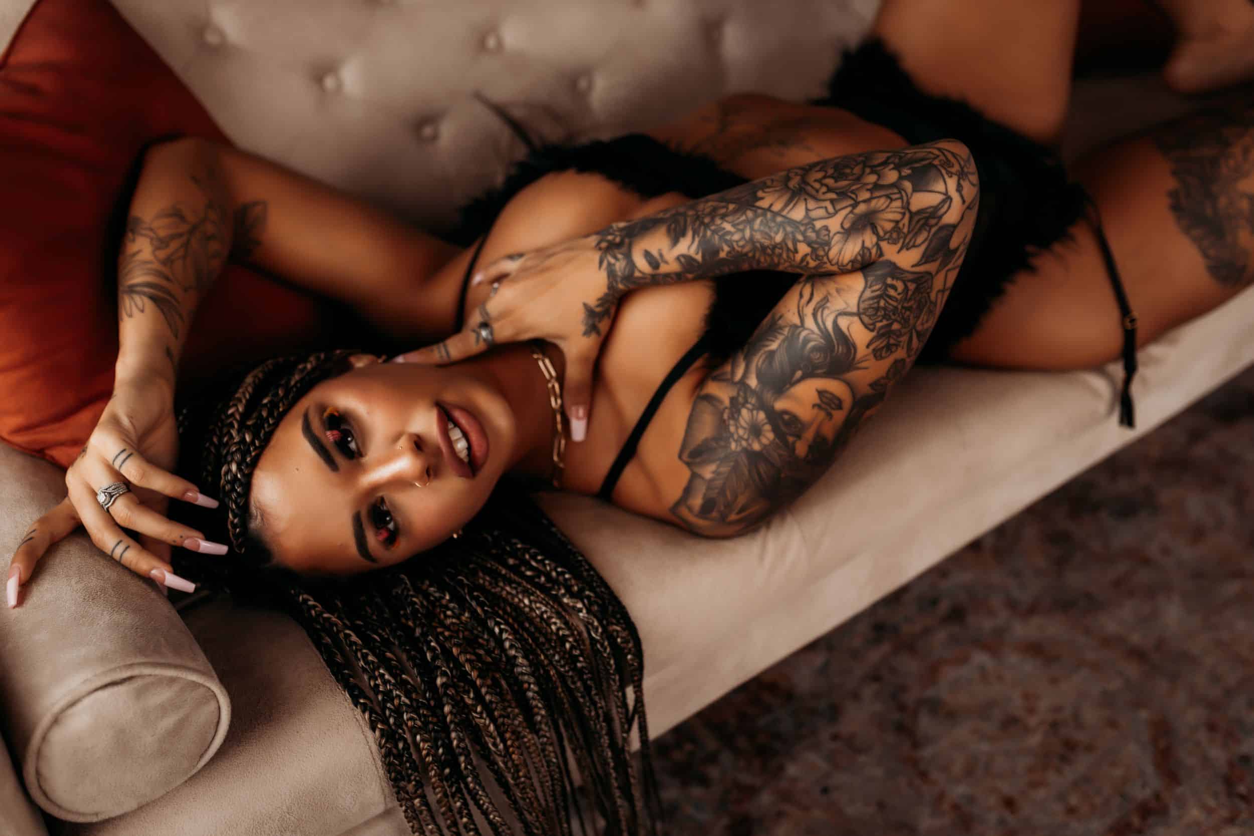 A girl with braids and tattoos lying on a sofa for an all-things boudoir photoshoot.