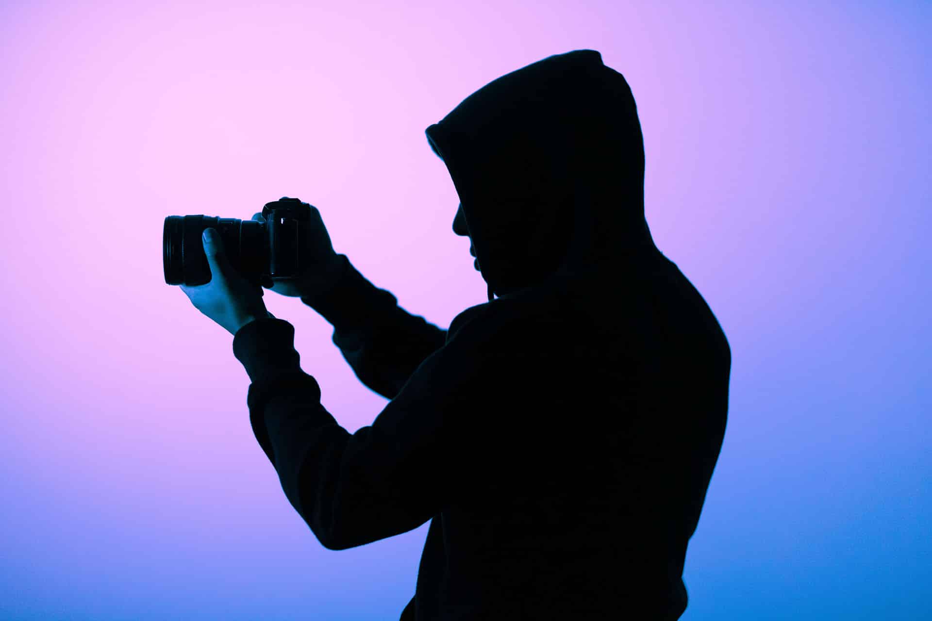 A man holding a camera against a gradient background.