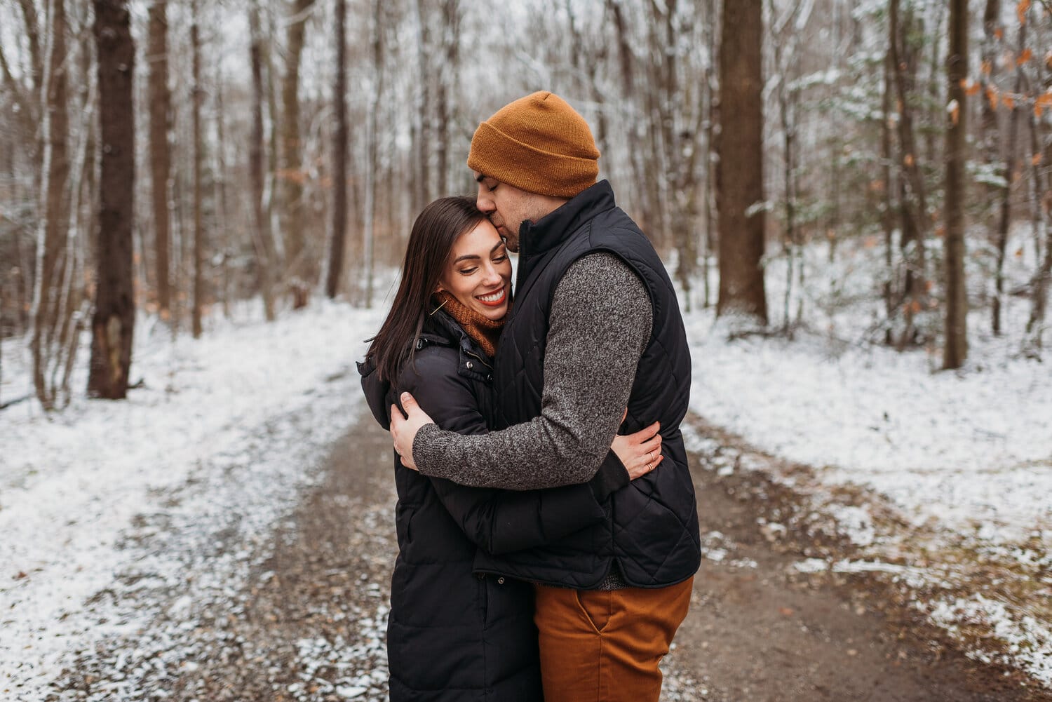 Couple standing in a winter forest, with the man embracing the woman