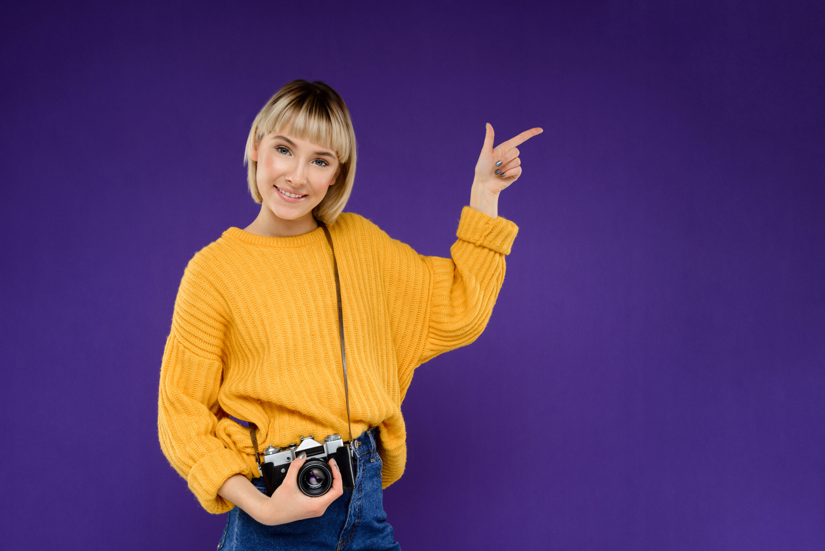 Close-up portrait of a young girl in a yellow sweater pointing with her finger on a purple background